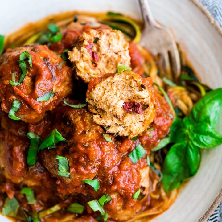 overhead view of a Healthy Turkey Meatball cut in half on top of zucchini noodles with pasta sauce and garnished with fresh chopped basil