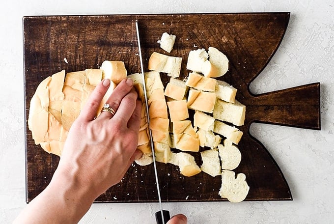 overhead view of hands cutting half a loaf of french bread on a wooden cutting board to make Homemade Croutons