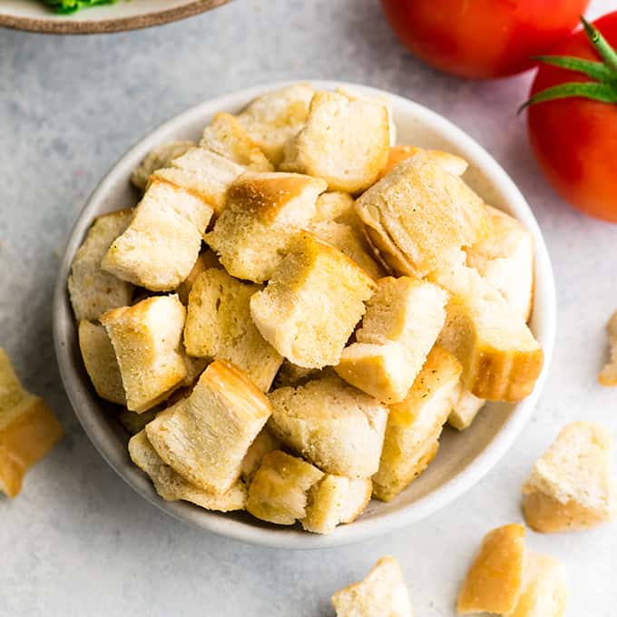 overhead view of a bowl of Homemade Croutons with a salad, tomatoes and more croutons around it