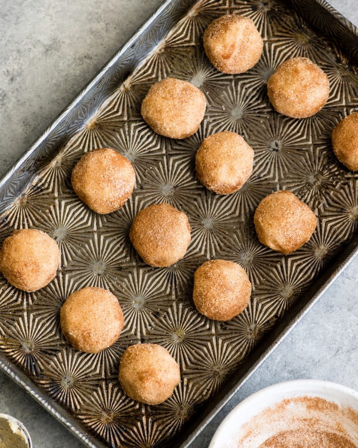 overhead view of 12 Snickerdoodle Cookie dough balls on a baking sheet that have been rolled in cinnamon sugar before baking