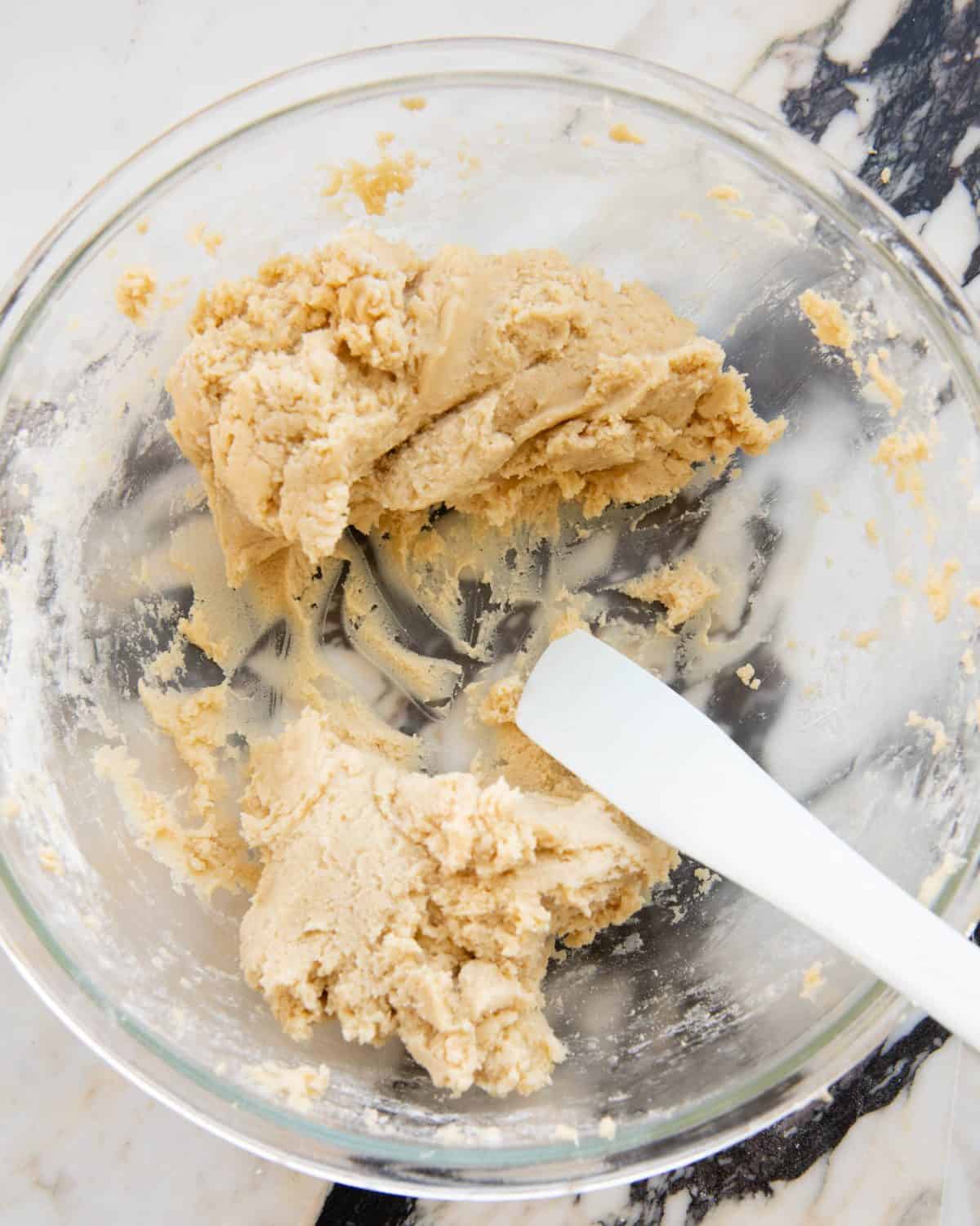 making cut out sugar cookies recipe - dough in a large glass bowl divided into two portions with a silicone spatula on a marble surface