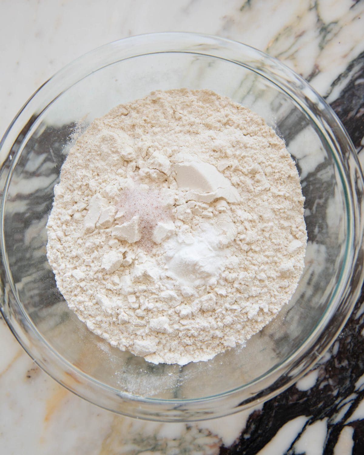 making cut out sugar cookies recipe - flour, baking powder and salt in a glass mixing bowl on a marble surface before mixing
