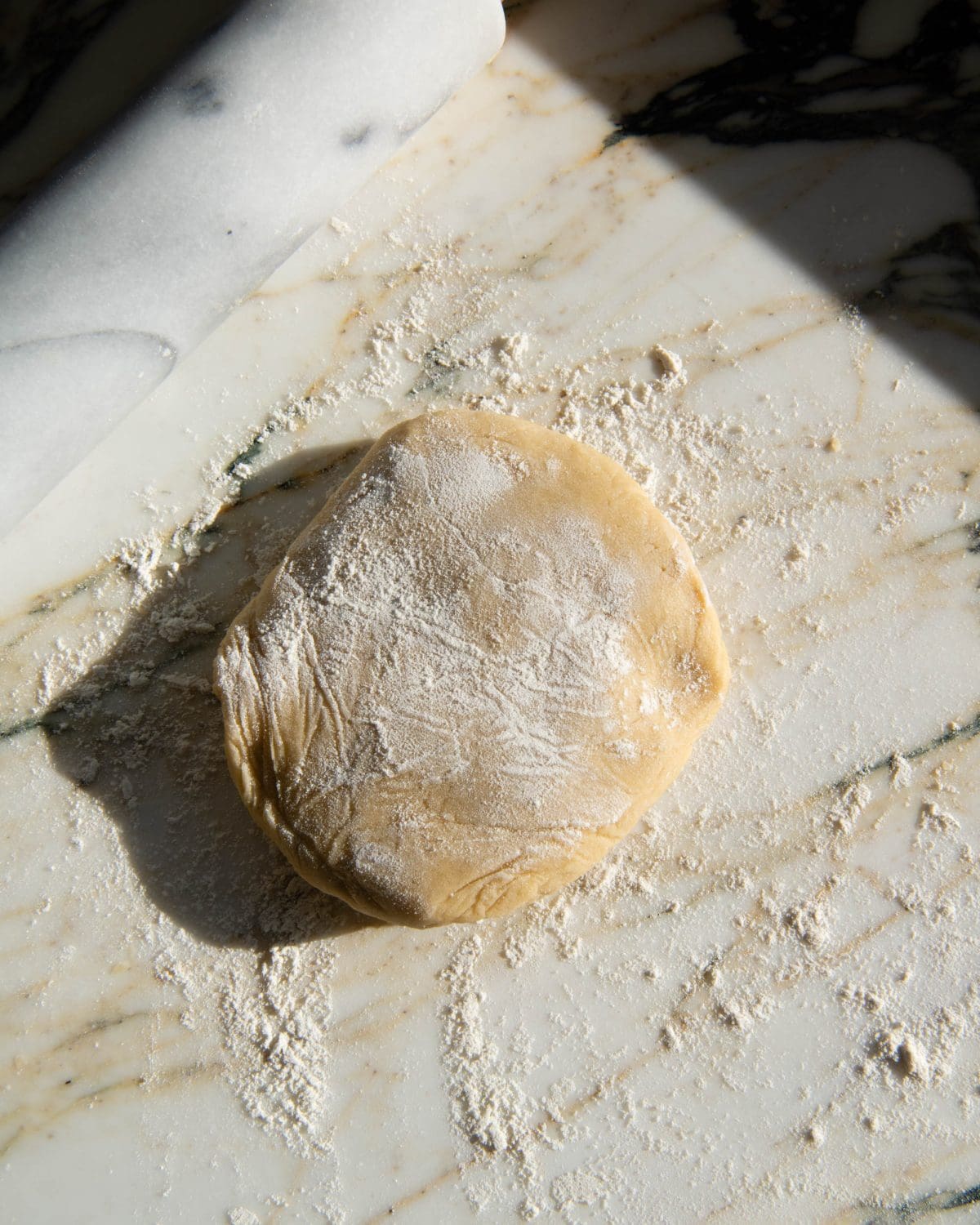 making cut out sugar cookies recipe - a disc of dough covered in flour ready to be rolled on a marble surface with a marble rolling pin in the top left corner.