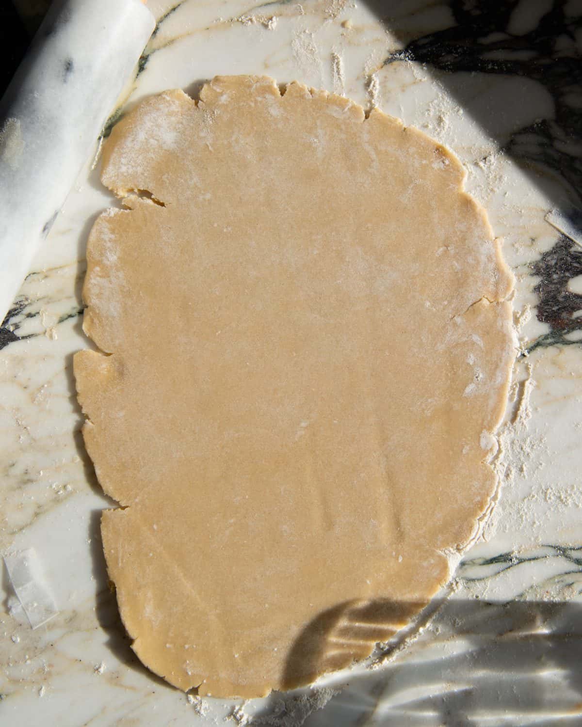 making cut out sugar cookies recipe - dough rolled into an oval shape on a floured marble surface with a marble rolling pin in the left corner.