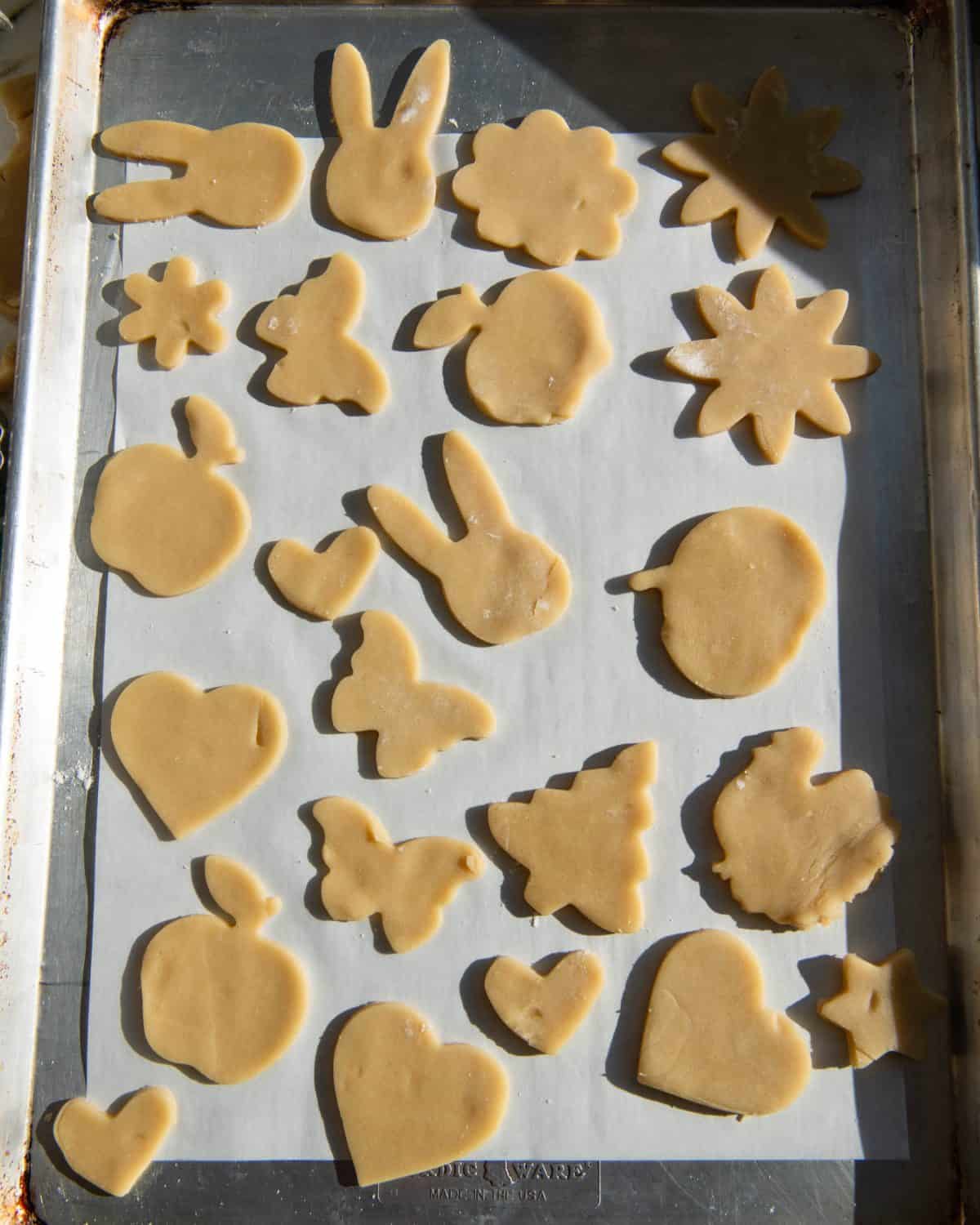 cut out sugar cookies on a baking sheet lined with parchment paper before baking. Cut into shapes like bunnies, apples, flowers, hearts, butterflies, Christmas trees, pumpkins and turkeys.