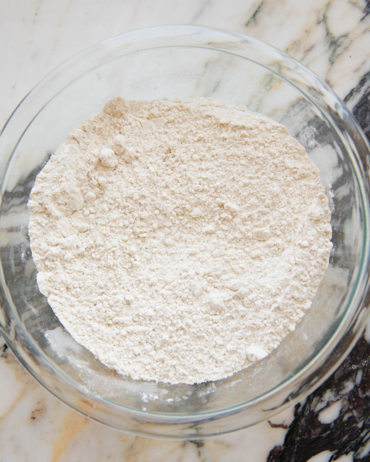 making cut out sugar cookies recipe - flour, baking powder and salt mixed together in a small glass bowl on a marble surface. 