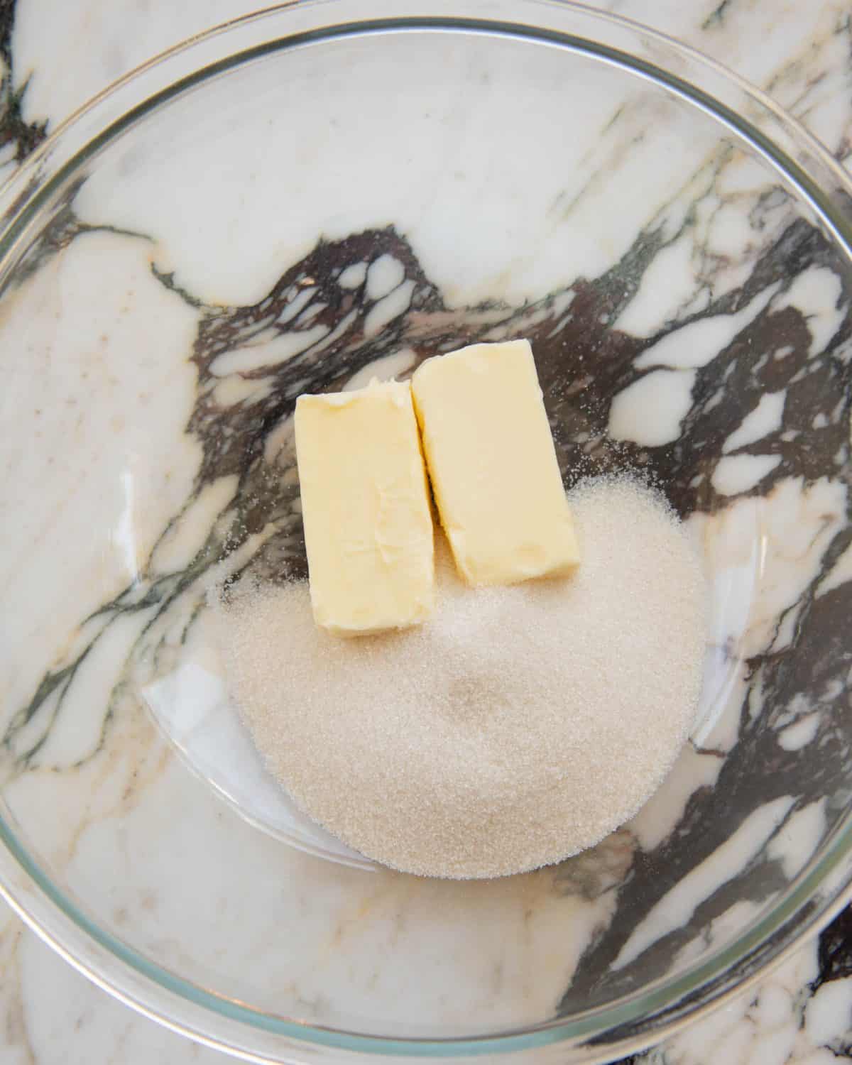 making cut out sugar cookies recipe - two sticks of butter and granulated sugar in a large glass mixing bowl on a marble surface