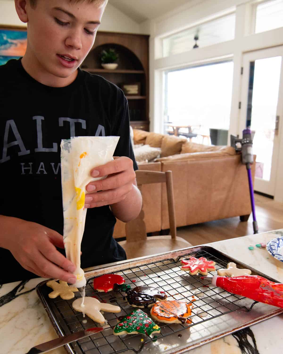 a teenage boy frosting a sugar cookie with a piping bag