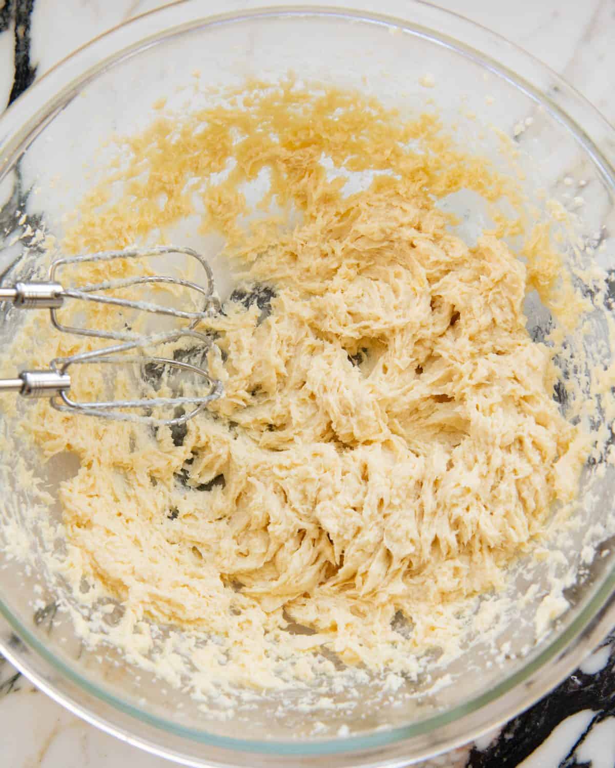 making cut out sugar cookies recipe - wet mixture beaten until light and fluffy in a large glass mixing bowl on a marble surface with two beaters from a handheld mixer also in the bowl.