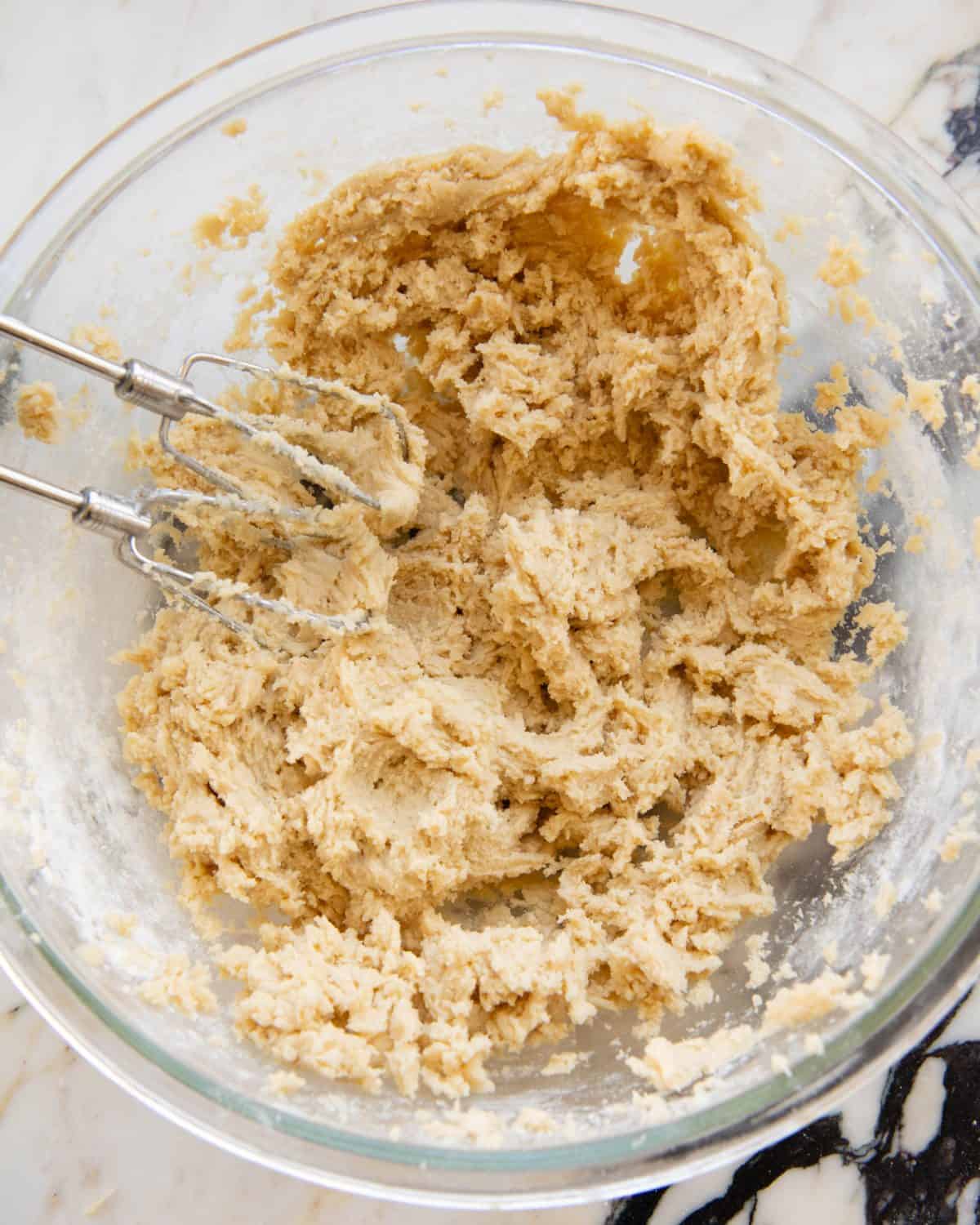 making cut out sugar cookies recipe - final cookie dough in a large glass bowl on a marble surface with two beaters also in the bowl. 