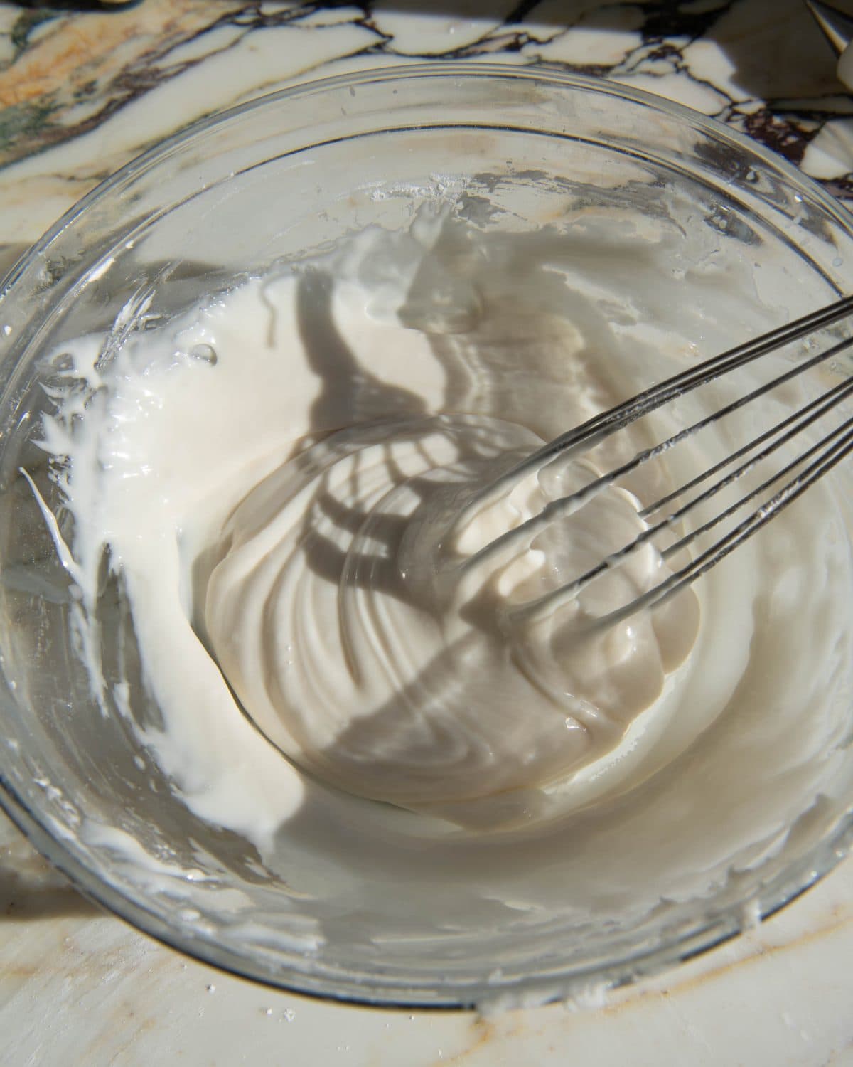 cut out sugar cookie frosting in a glass bowl on a marble surface after being whisked, the metal whisk is also in the bowl