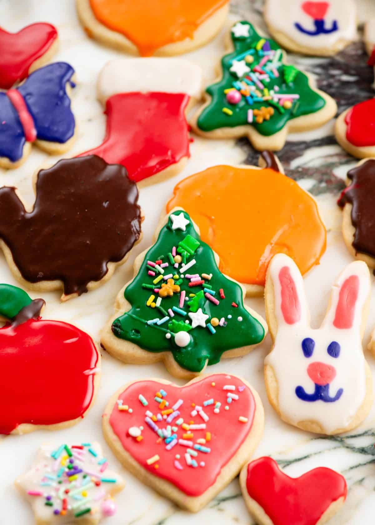 frosted cut out sugar cookies after the frosting has hardened on a metal surface in the shapes of hearts, Christmas trees, stockings, pumpkin, turkeys, bunnies and a butterfly.