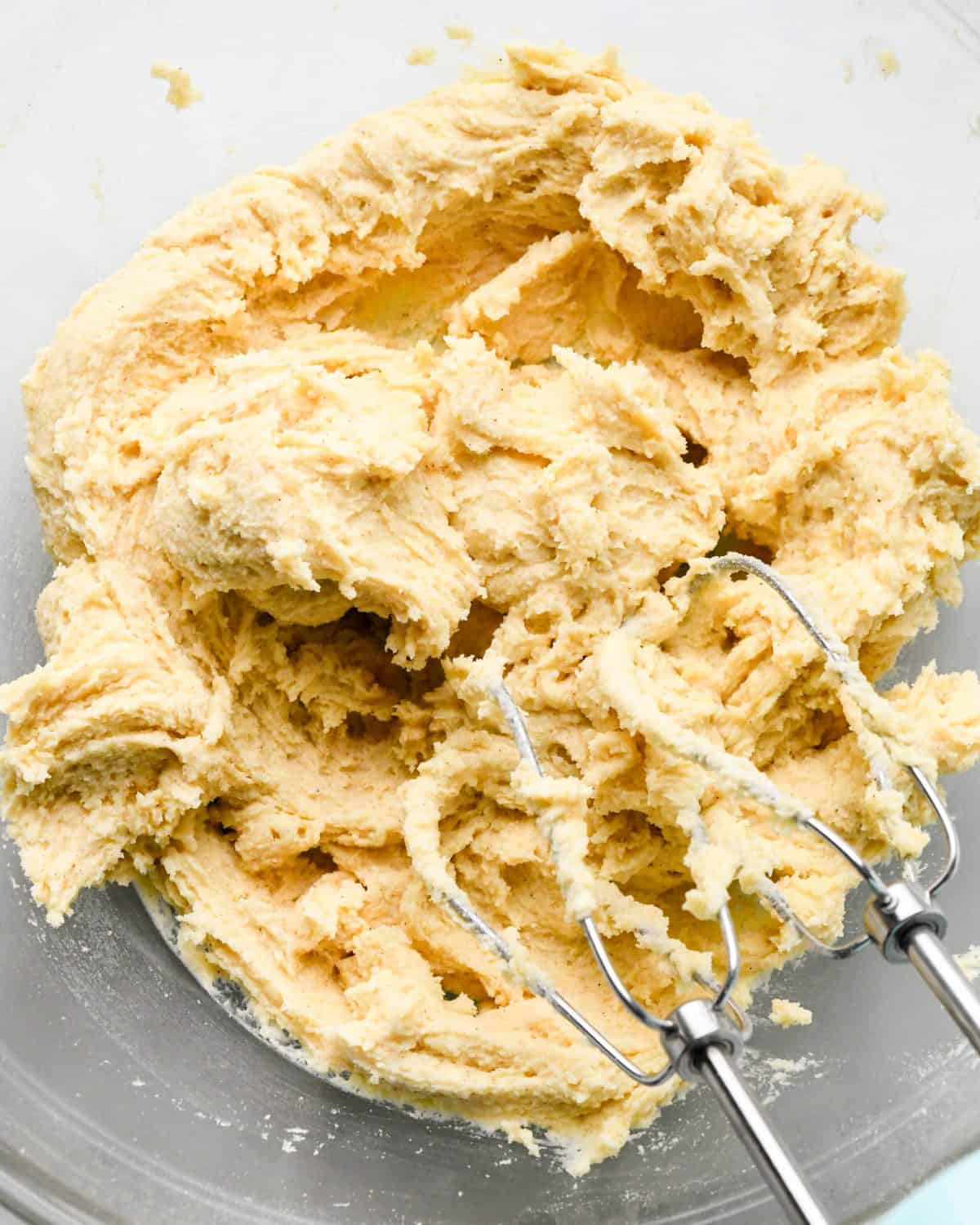 final snickerdoodles dough in a glass mixing bowl with two metal beaters in the dough