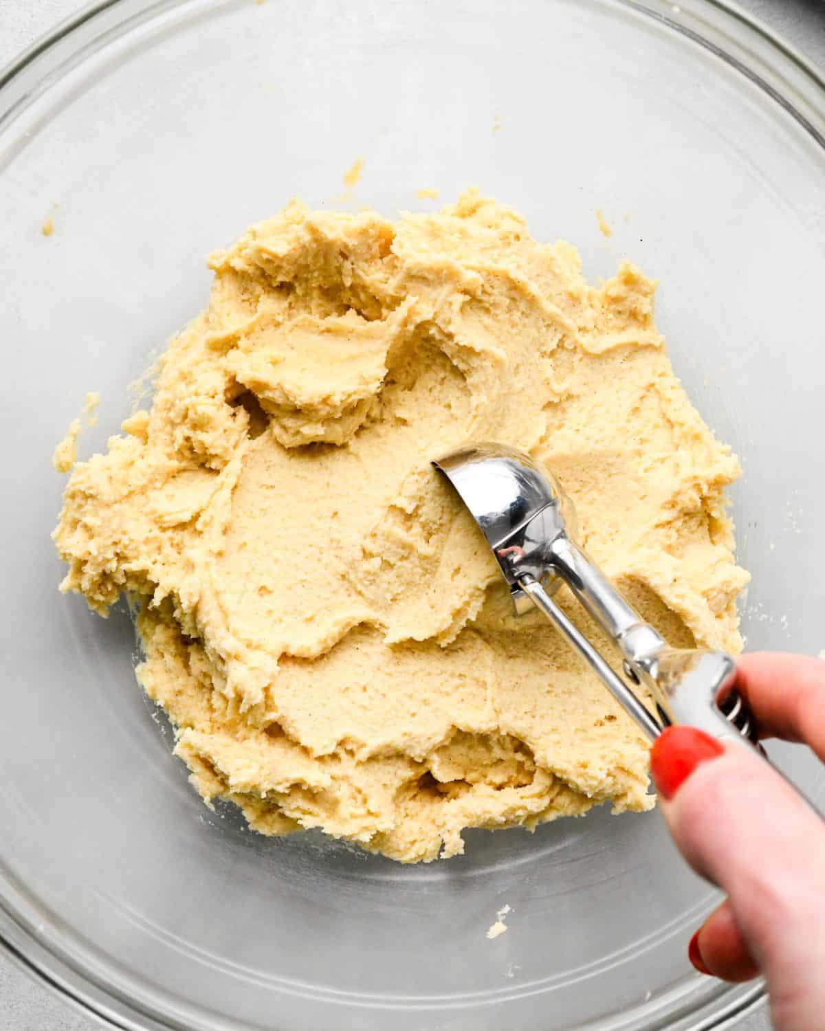 making snickerdoodles - a hand scooping snickerdoodle cookie dough out of a glass mixing bowl