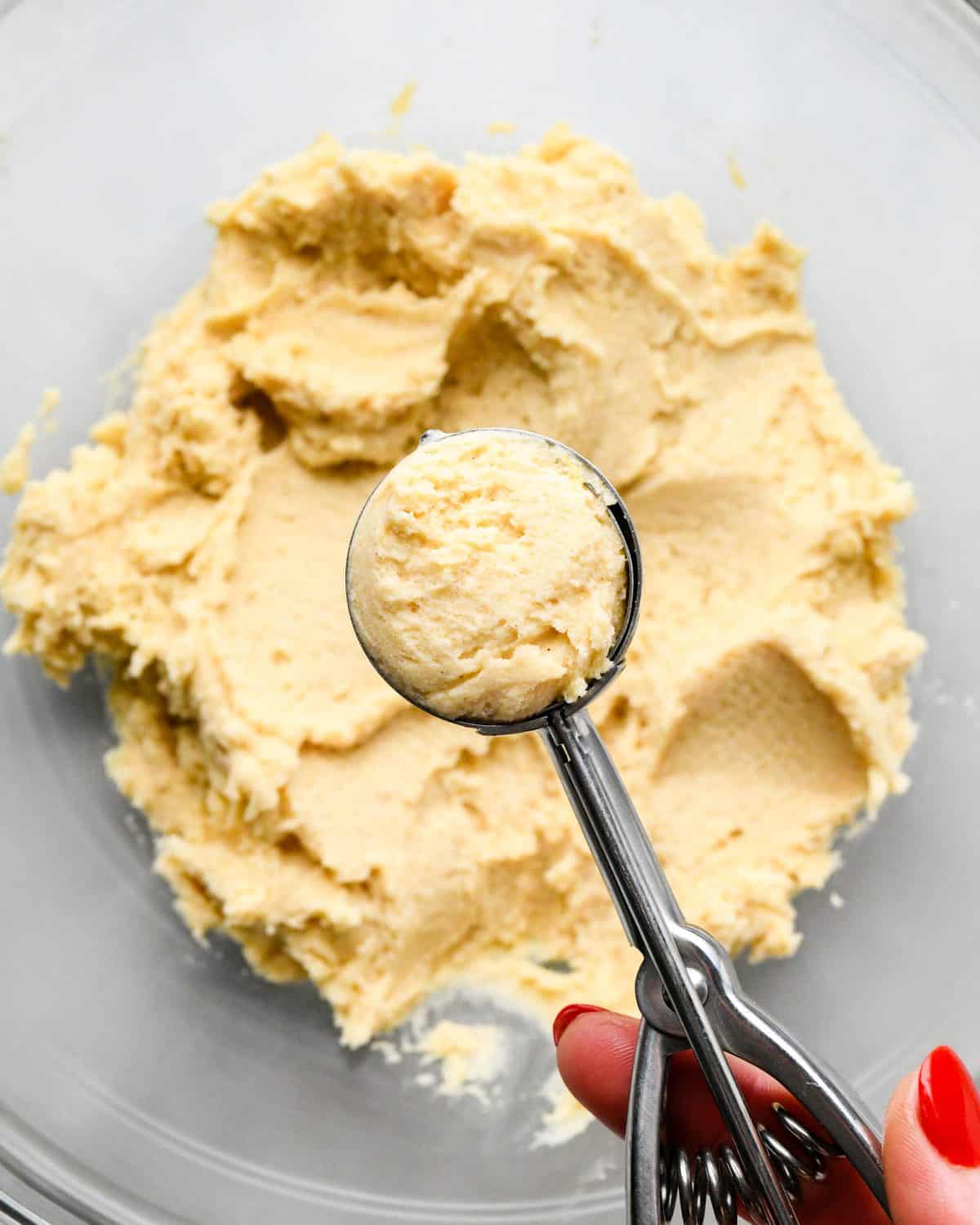 making snickerdoodles - cookie dough on a cookie scoop being held over a glass bowl of dough