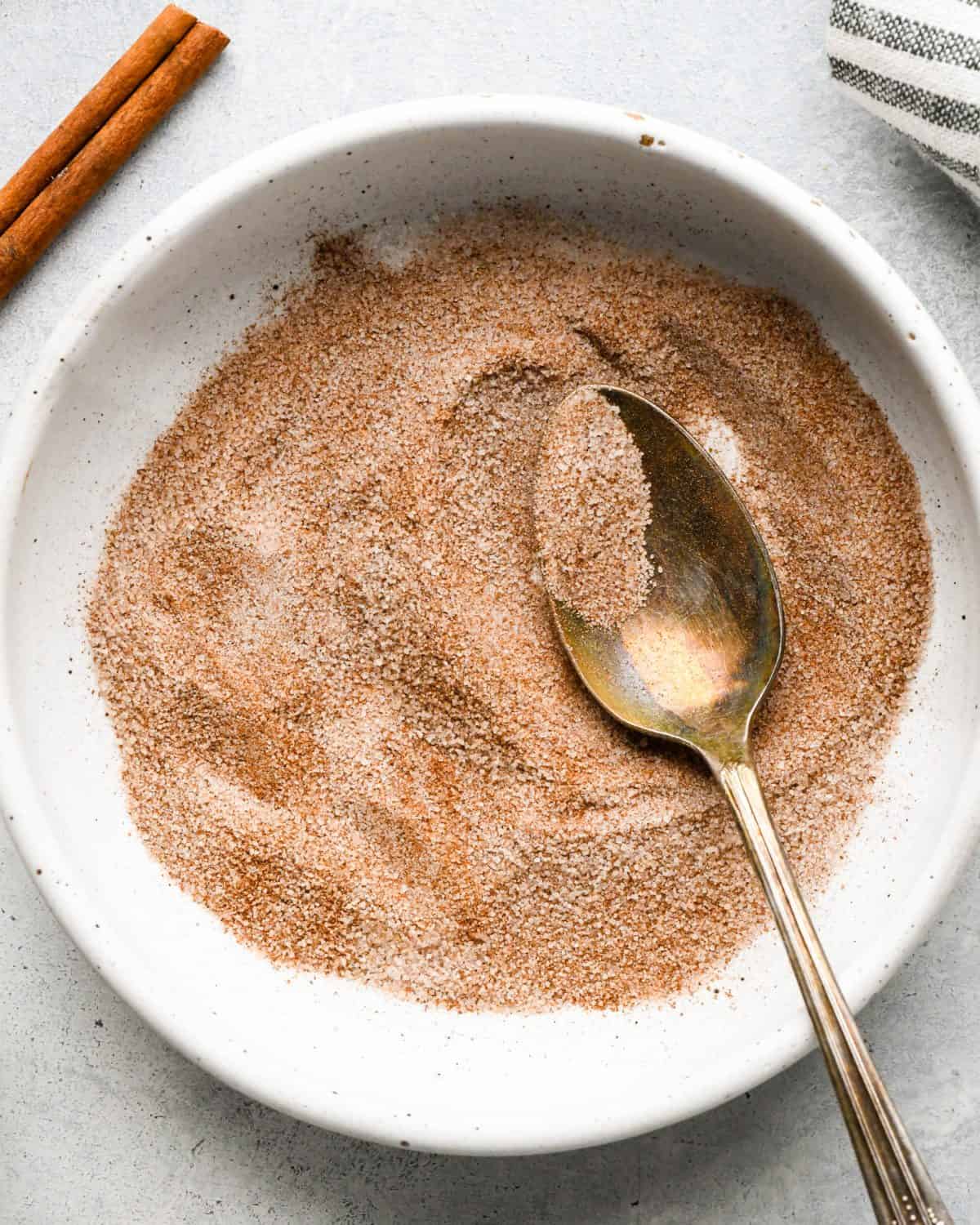 making snickerdoodles - cinnamon and sugar in a small white ceramic bowl with a metal spoon after mixing