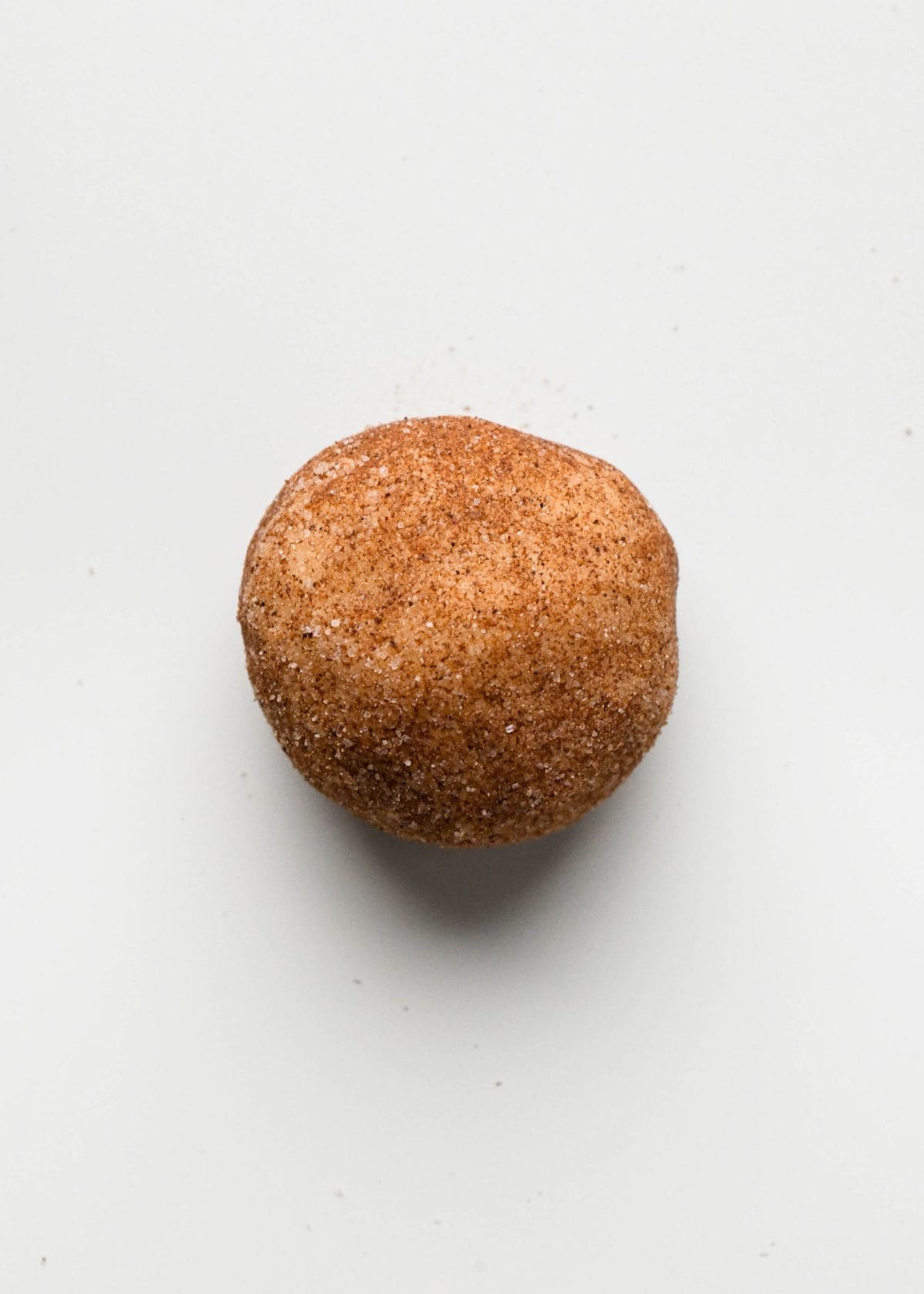 making snickerdoodles - close up photo of a snickerdoodle cookie dough ball on a baking sheet coated in cinnamon sugar