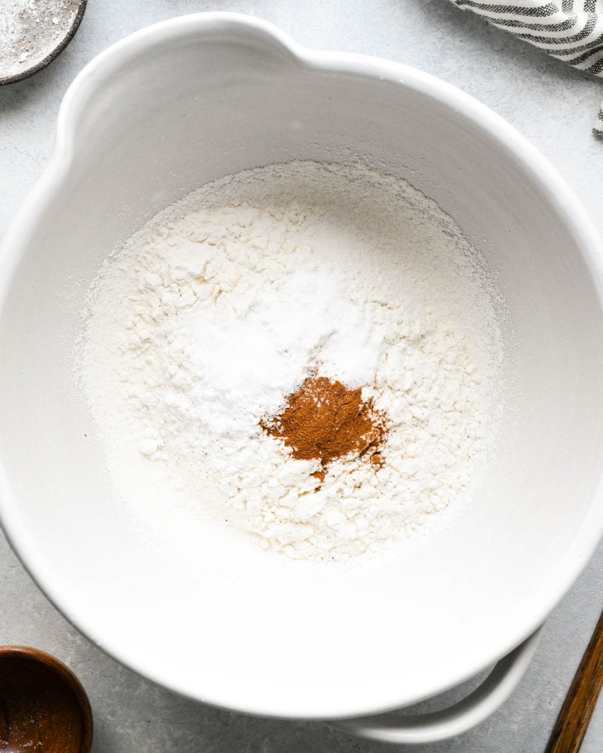 making snickerdoodles - sifted flour, baking soda, cream of tartar and cinnamon in a white ceramic bowl before mixing