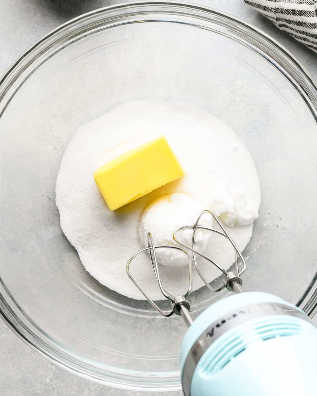 making snickerdoodles - white sugar, a stick of butter and shortening in a glass mixing bowl with a blue hand mixer before mixing
