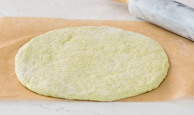 front view of a Zucchini Pizza Crust rolled into a circle on a piece of brown parchment paper