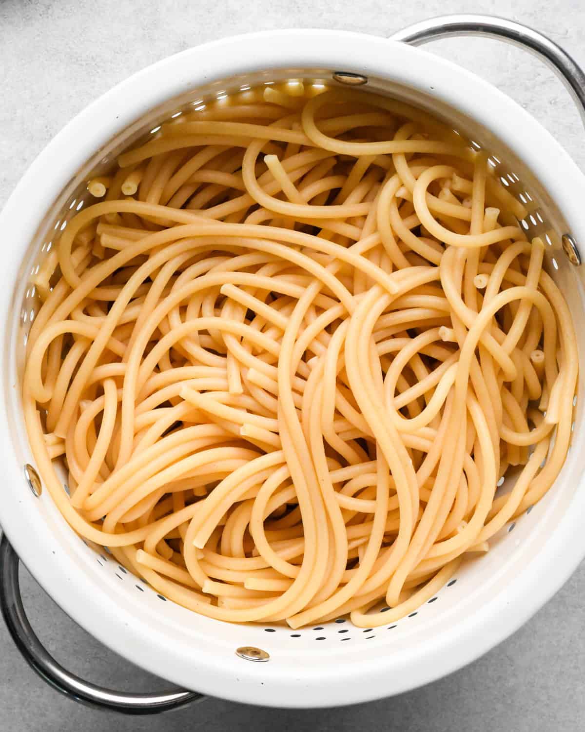 cooked pasta in a white colander with silver handles making pesto pasta 