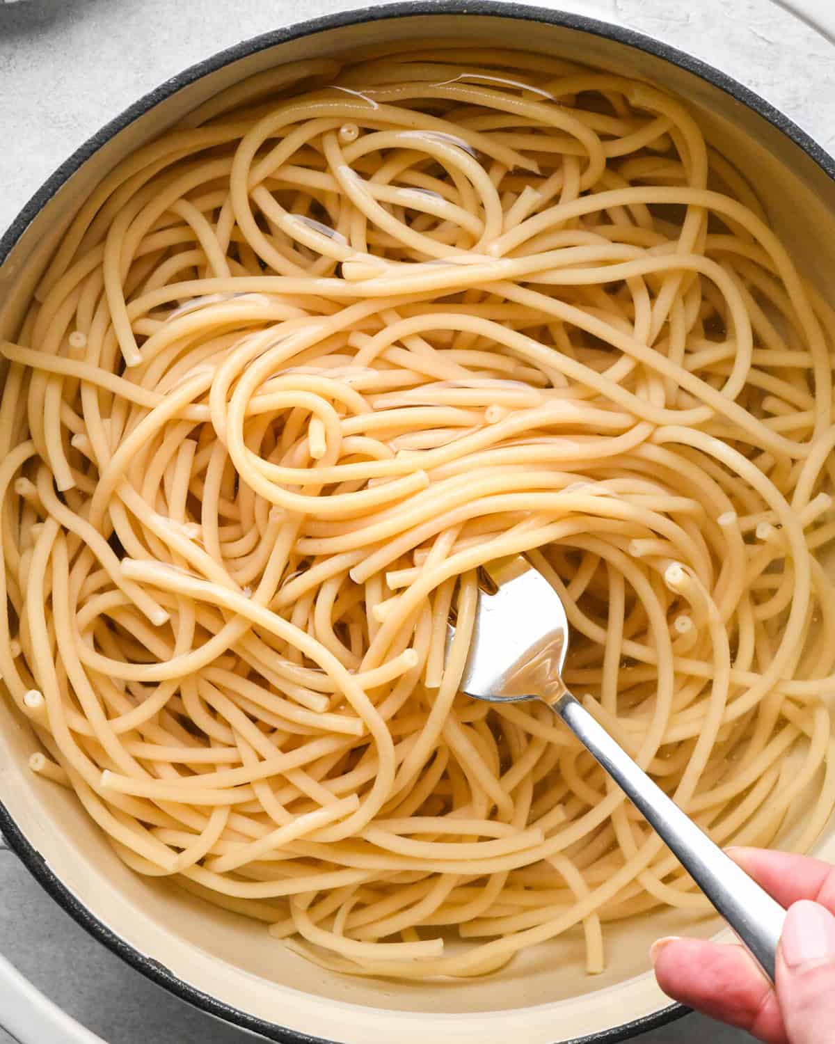 cooked pasta in a pot of water with a fork showing the cooked noodles making pesto pasta