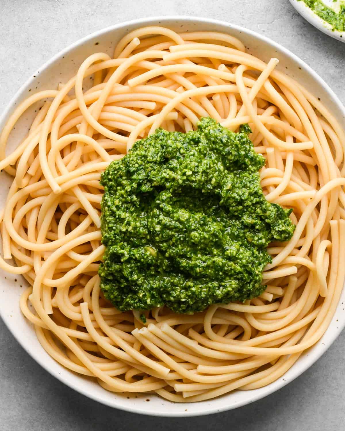 pesto sauce added on top of cooked pasta in a white bowl before mixing, making pesto pasta. 