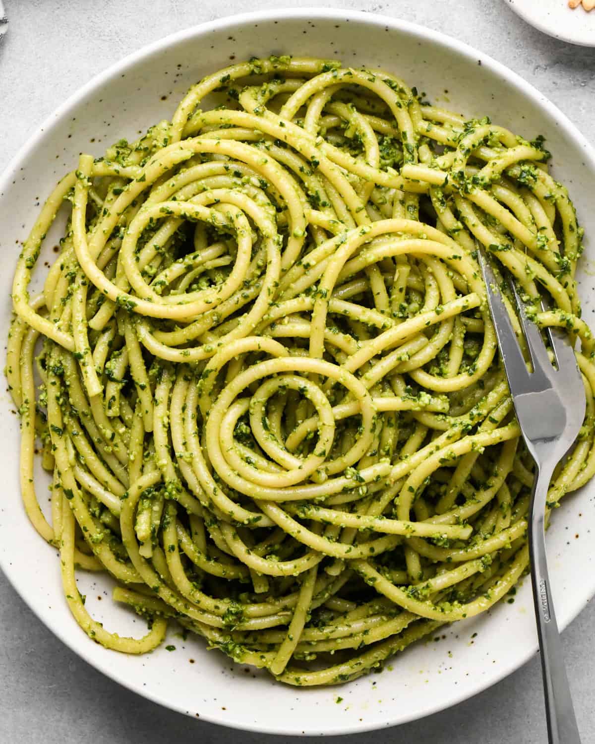 pesto pasta after sauce and noodles have been combined in a white bowl with a silver fork on a gray surface