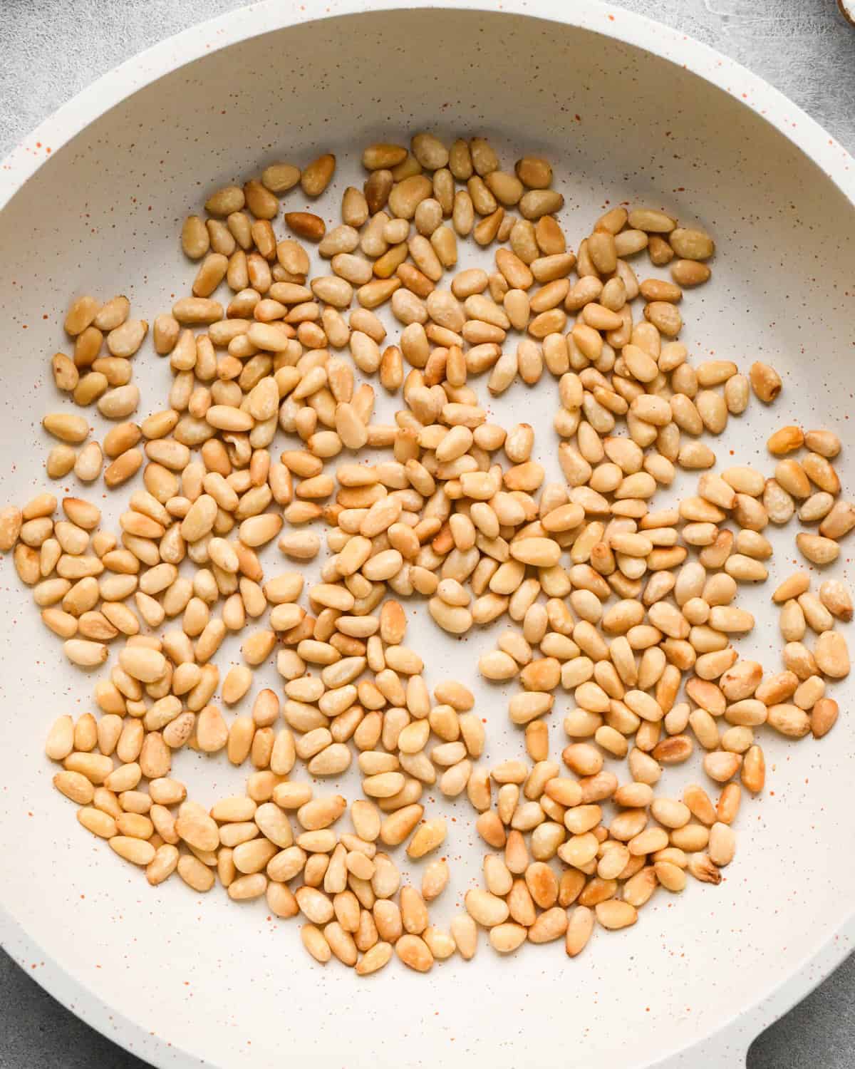 toasted pine nuts in a small, white skillet making this pesto and pasta recipe