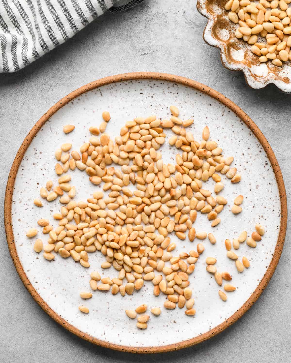 toasted pine nuts on a ceramic plate and in a ceramic bowl to be used to make this pesto pasta recipe
