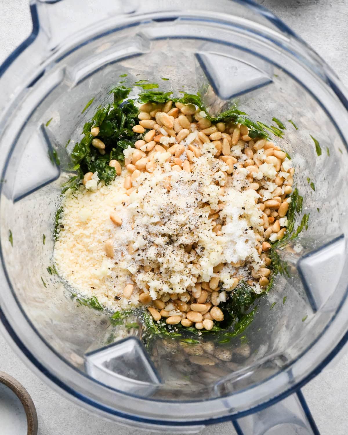 making pesto pasta sauce in a blender pine nuts, parmesan cheese, salt, pepper and minced garlic added to the basil in the blending container before blending