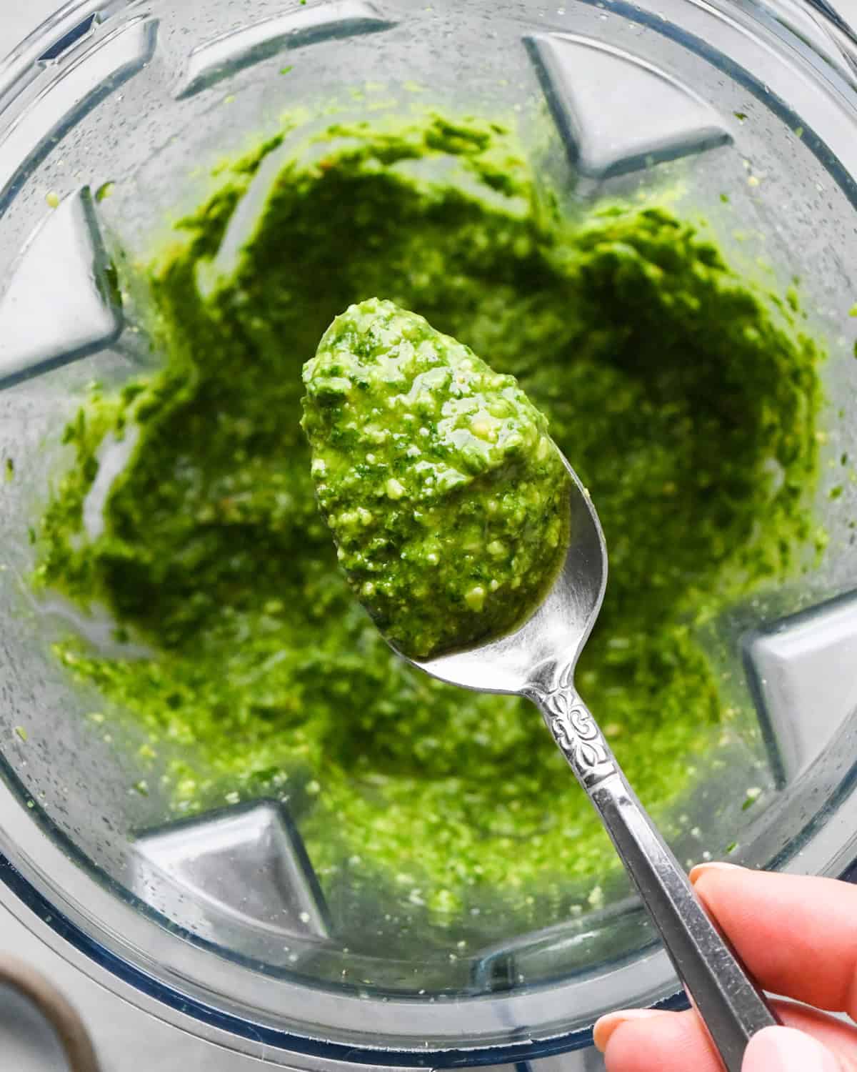 a spoon holding a scoop of pesto sauce over pesto sauce in a blending container to make pesto pasta 