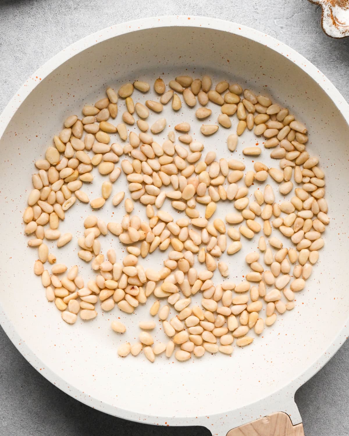 uncooked pine nuts in a small, white skillet before toasting making this pesto and pasta recipe
