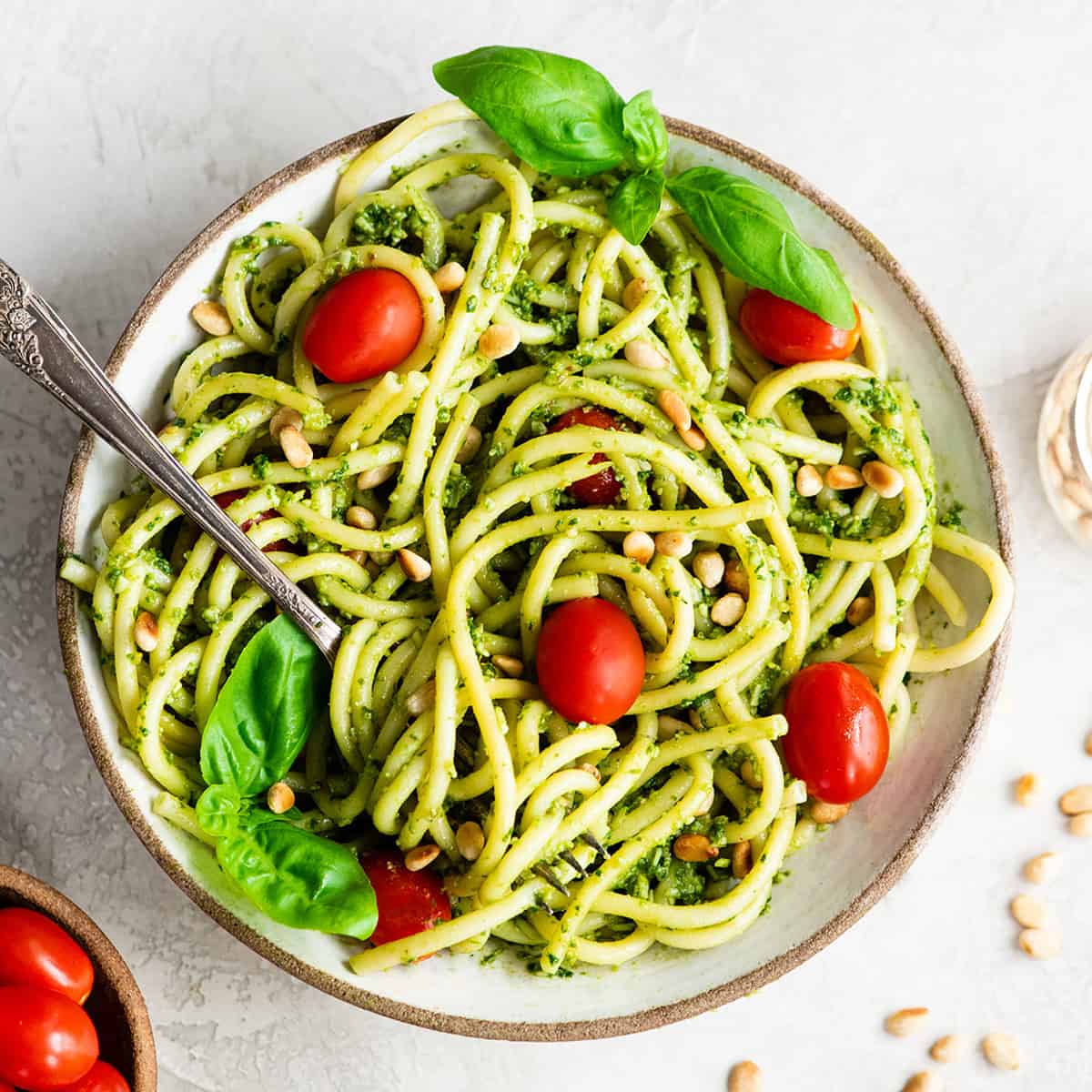 a bowl of pesto pasta garnished with tomatoes, pine nuts and basil