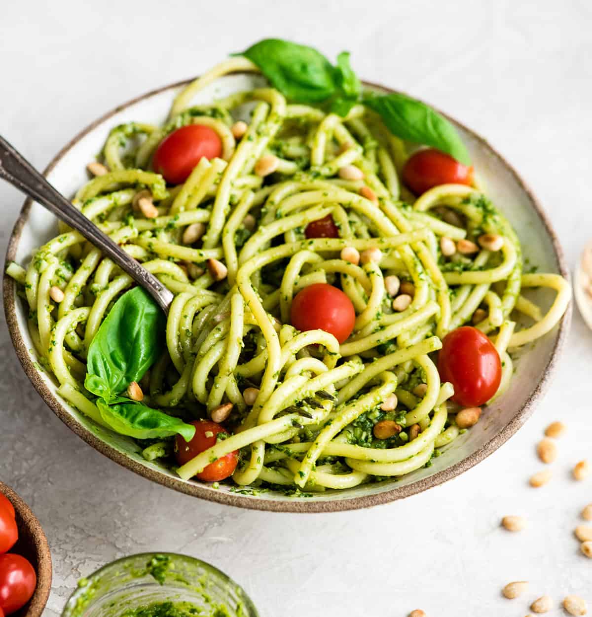 Overhead/front view of a bowl of Pesto Pasta with tomatoes, fresh basil and toasted pine nuts and a fork with a twirl of pasta on it