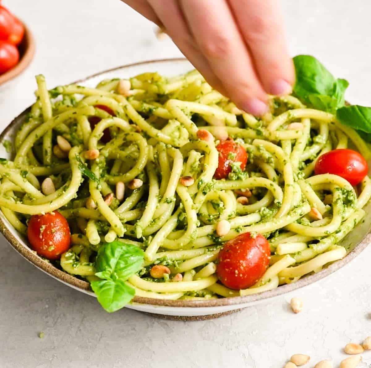 pine nuts being sprinkled over a bowl of pesto pasta