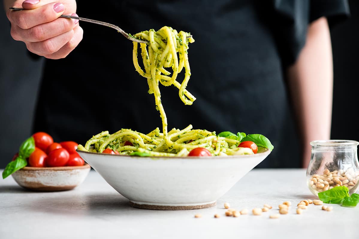 front view of a bowl of pesto pasta and a fork twirling a bite of it and lifting it out of the bowl