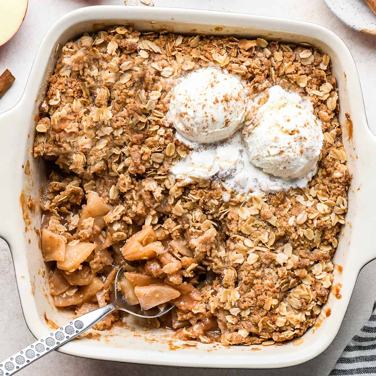 apple crisp in a baking dish with vanilla ice cream and a spoon