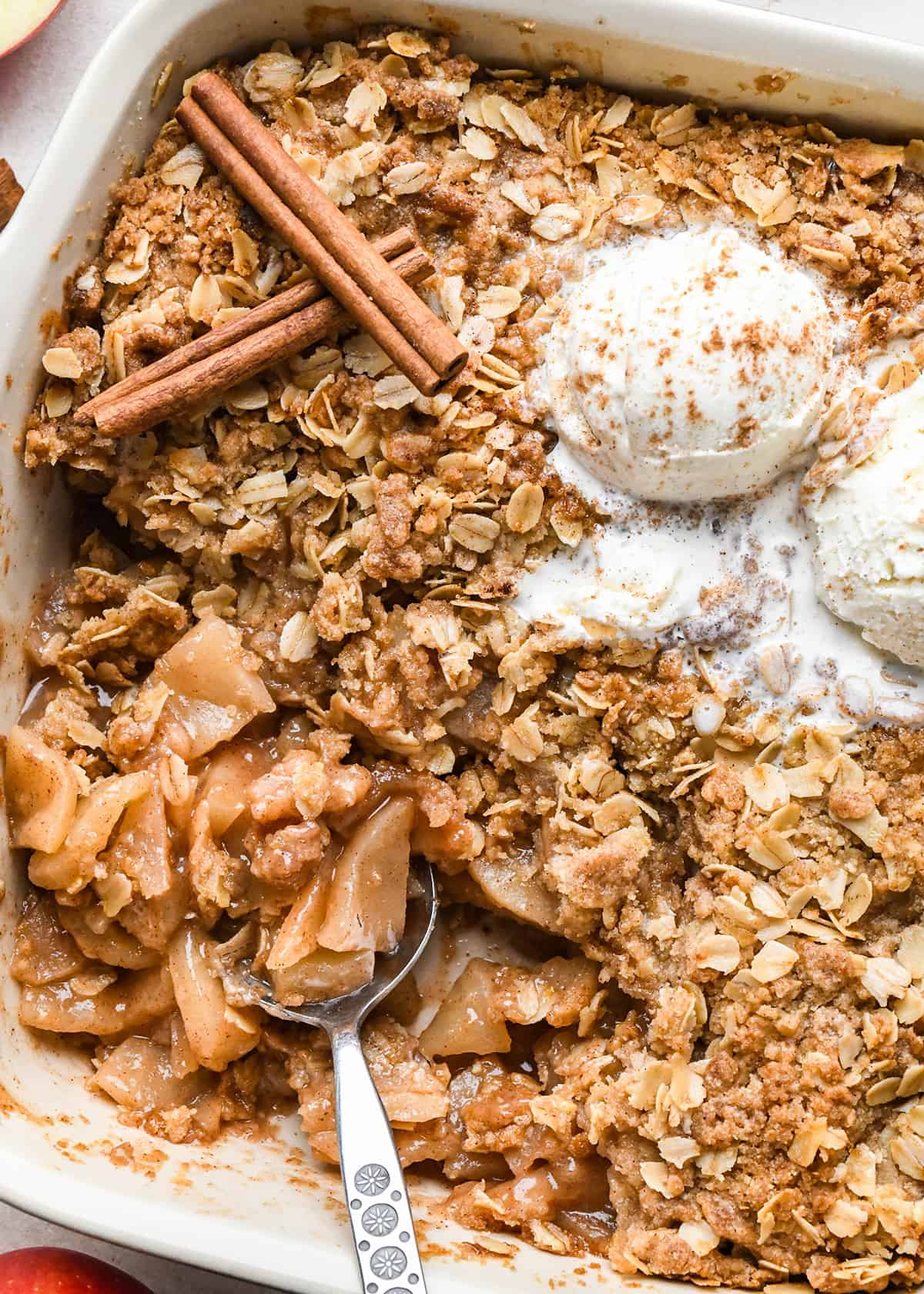 apple crisp in a baking dish with vanilla ice cream and a spoon taking a scoop