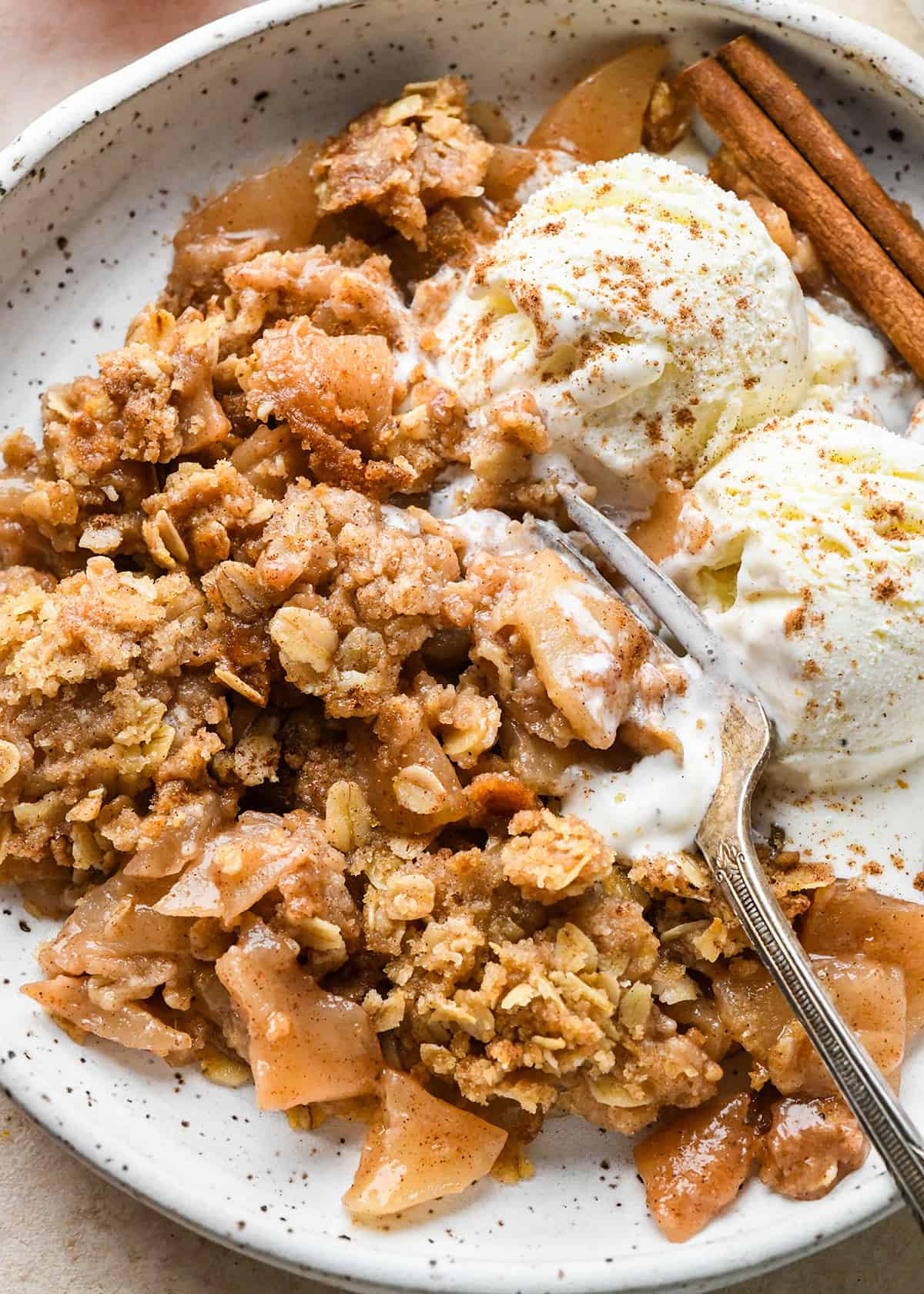 up close photo of apple crisp on a plate with ice cream and a fork