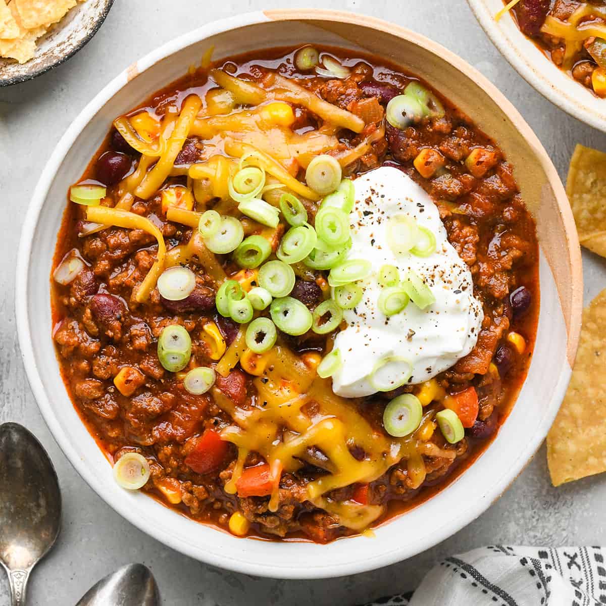 a bowl of chili topped with sour cream, cheese and green onions 