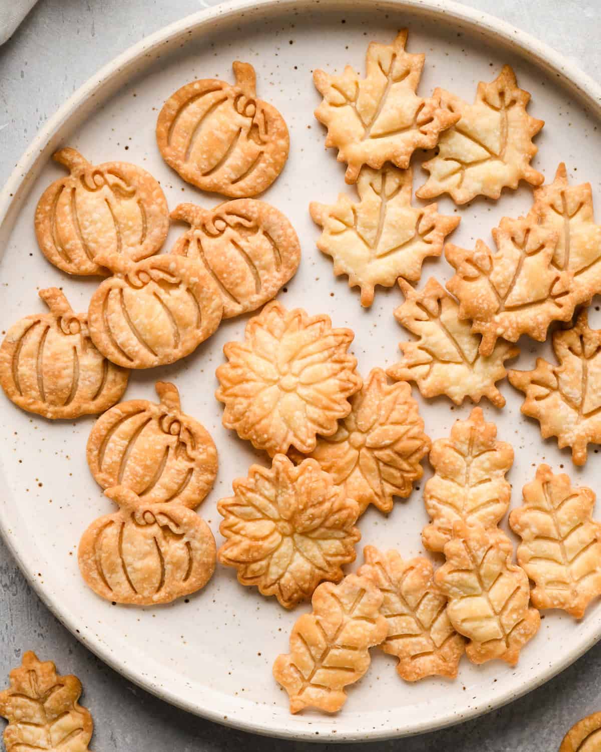 baked pie crust shapes in the shapes of flowers, pumpkins and leaves on a plate 