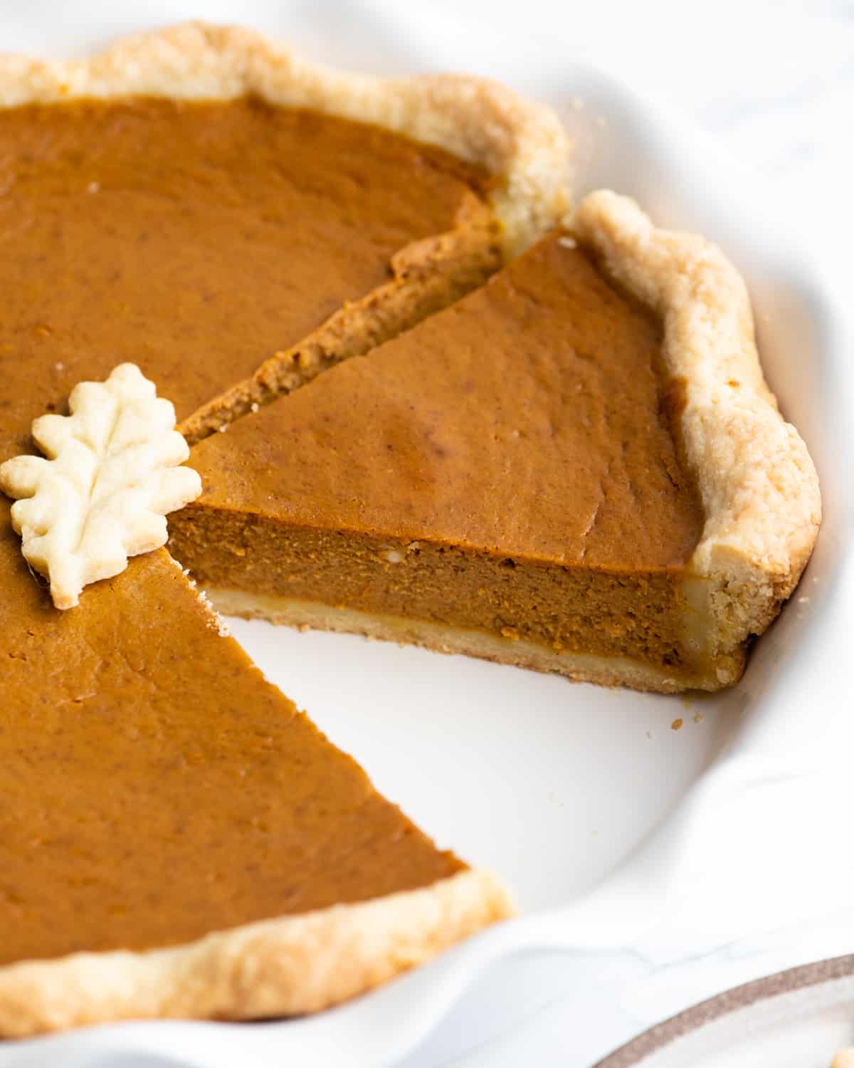 Pumpkin pie in a pie dish with a slice cut out 
