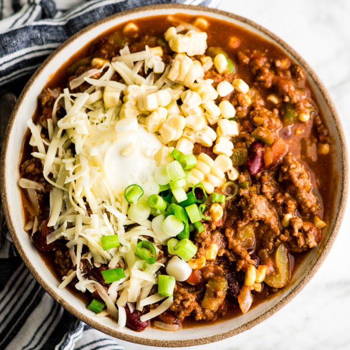 a bowl of beef chili topped with fresh corn, cheese, sour cream and green onions 