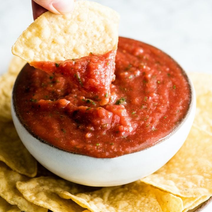 front view of a chip being dipped into a bowl of homemade salsa