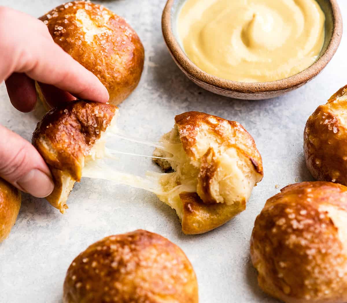 front view of a hand pulling apart a cheese-stuffed pretzel bite with a melty cheese pull