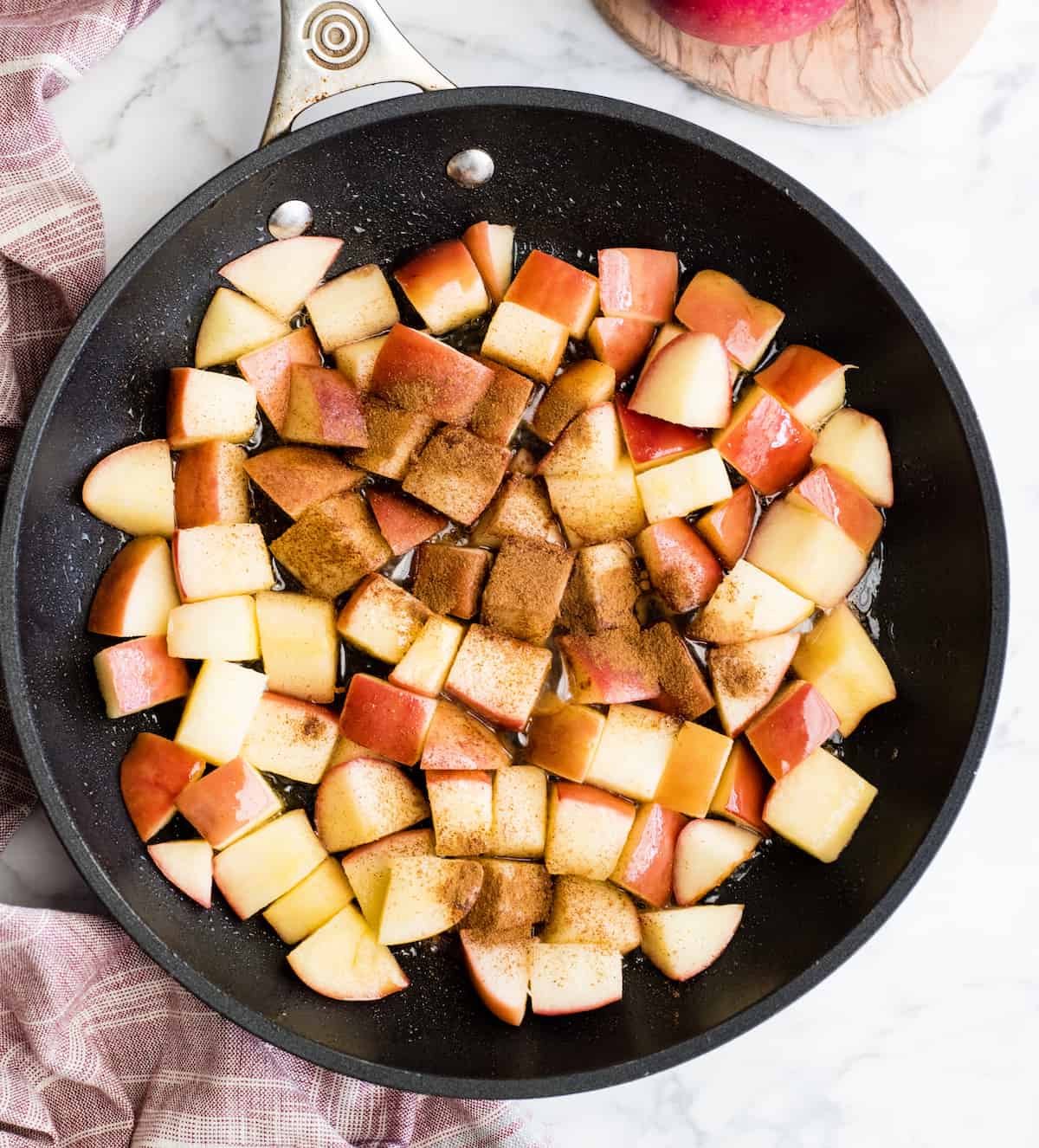 Overhead view of adding cinnamon to apples in a black fry pan showing how to make cinnamon apples