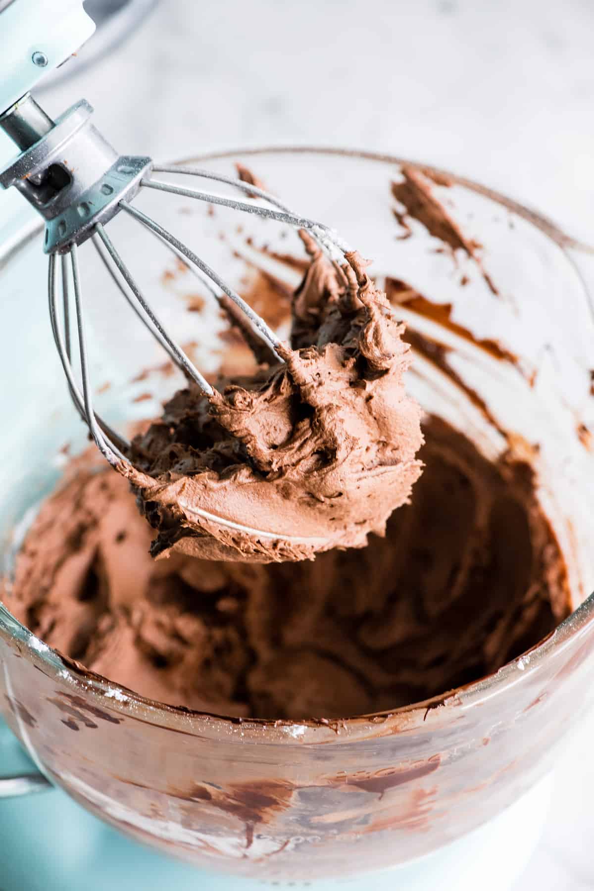 up close view of chocolate frosting on a wire whisk beater over a mixing bowl