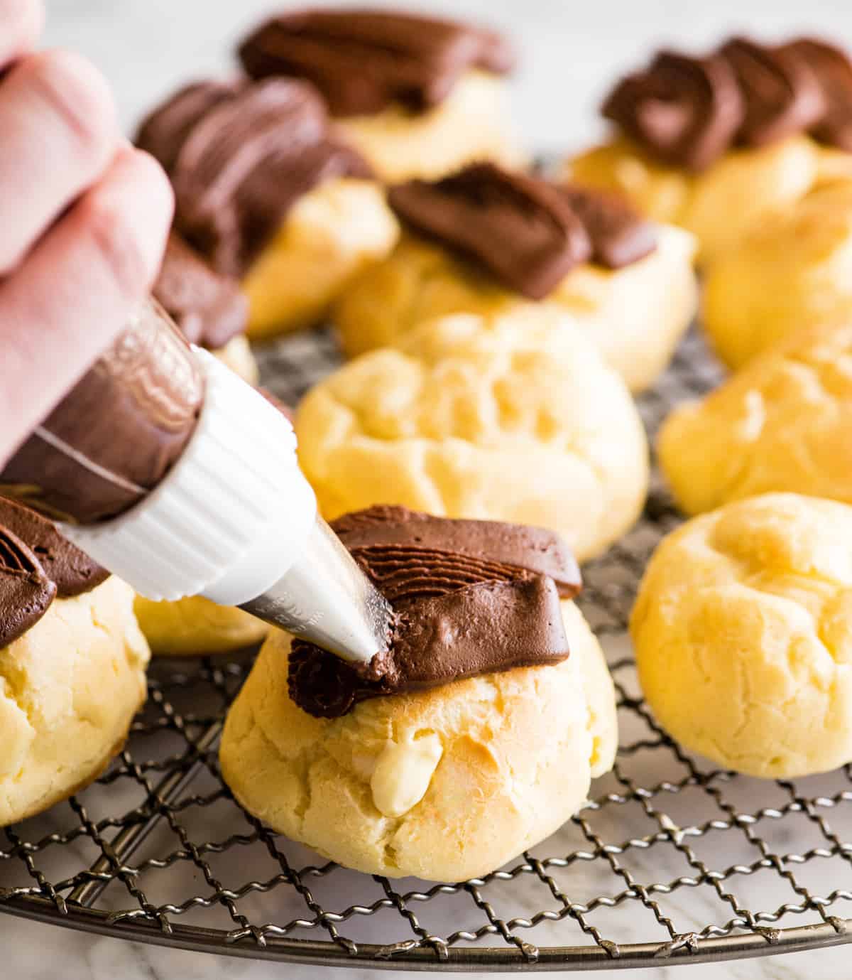 front view of an eclair being frosted with chocolate frosting