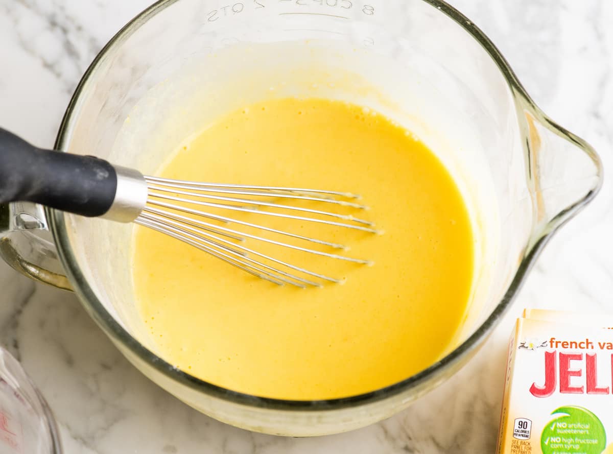 overhead view of a whisk mixing pudding and milk together in a glass bowl showing how to make eclairs